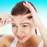 Young woman checking her wrinkles on forehead.