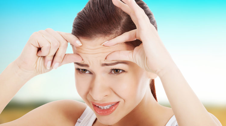 Young woman checking her wrinkles on forehead.